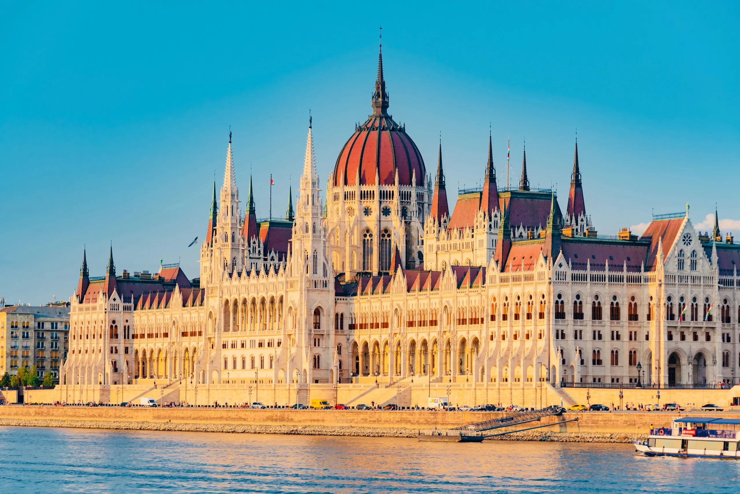 The Hungarian Parliament seen from across the Danube on a clear day, its Gothic Revival spires mirrored in the water.