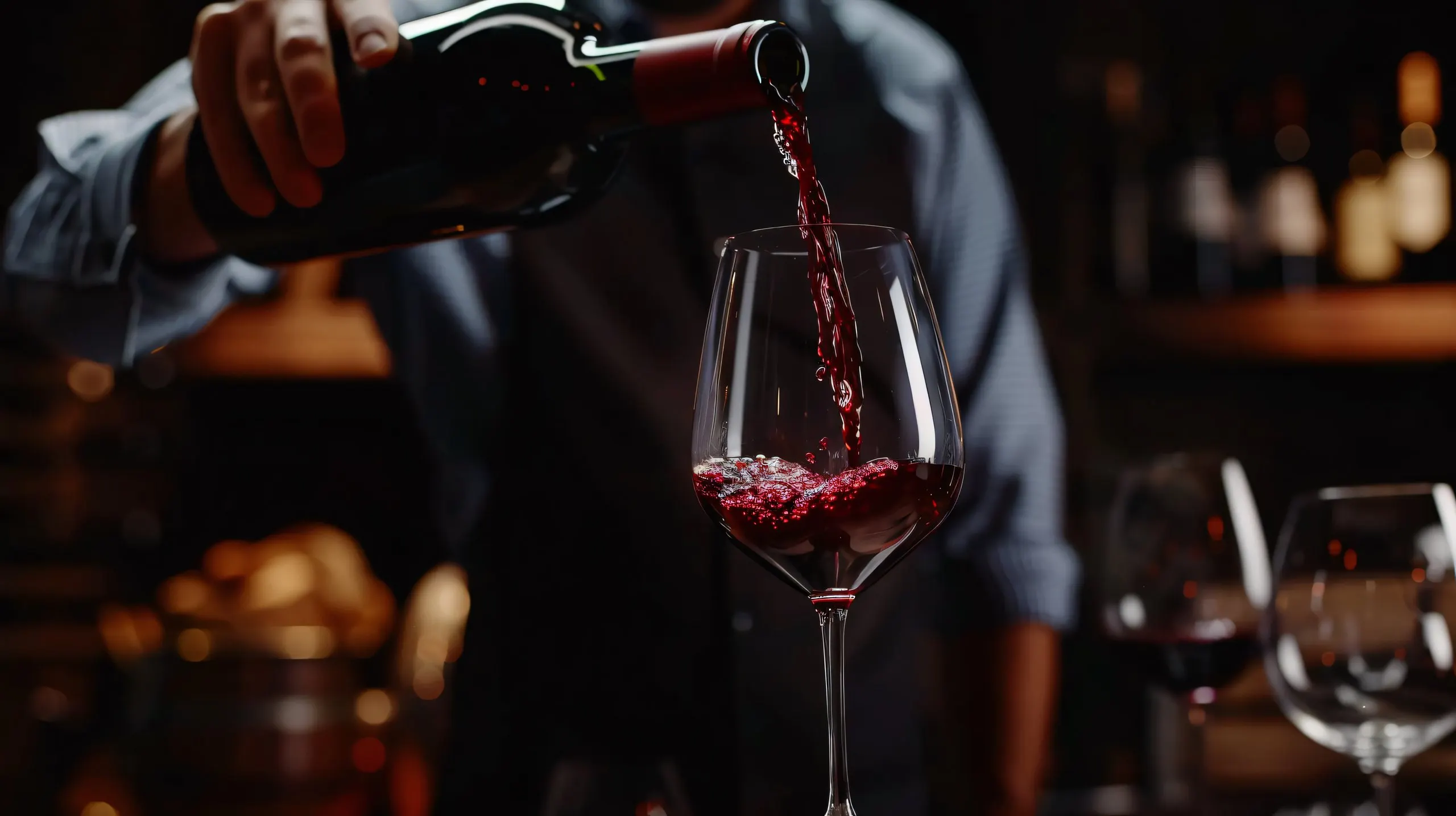 A sommelier pouring red wine into a glass in a dimly lit wine bar.